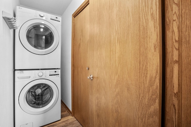 clothes washing area with wood finished floors, stacked washing maching and dryer, and laundry area