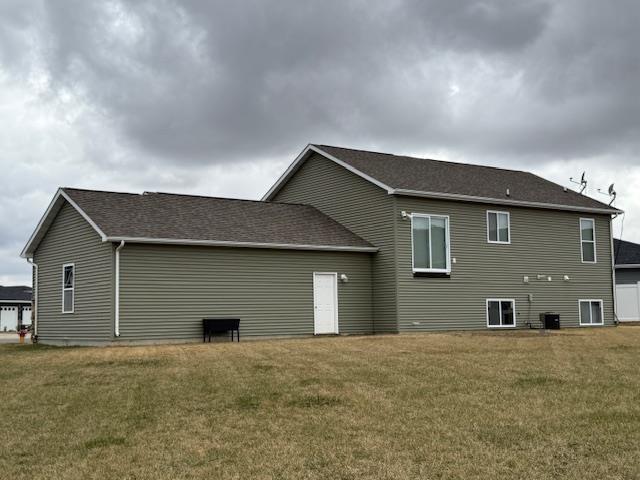 38 Mulberry Loop, Minot, ND 58703 - rear view of house with a lawn, central AC unit, and roof with shingles