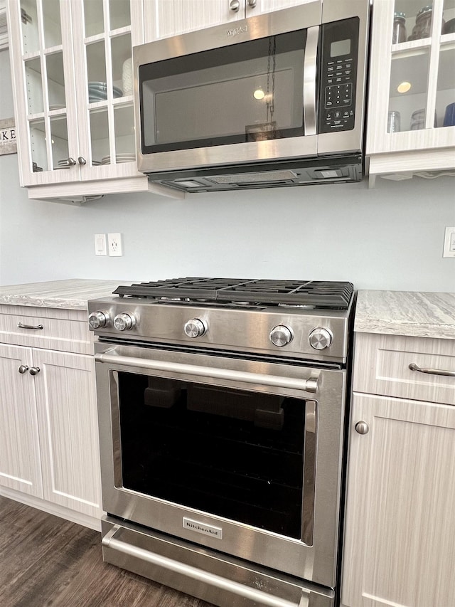 details featuring dark wood finished floors, glass insert cabinets, and appliances with stainless steel finishes