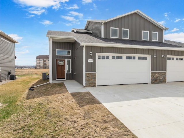 view of front facade with cooling unit, driveway, stone siding, and a shingled roof