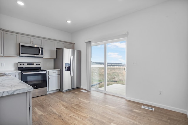 kitchen featuring appliances with stainless steel finishes, visible vents, gray cabinetry, light wood-style floors, and baseboards