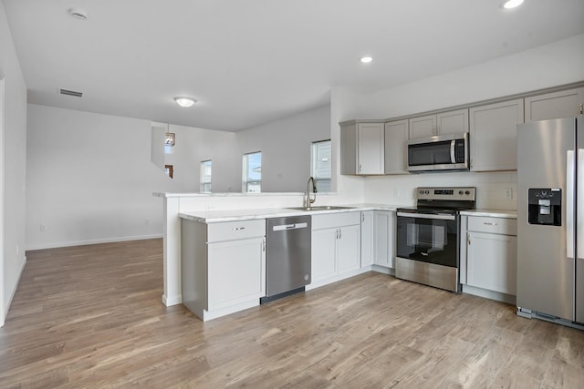 kitchen featuring light wood-style flooring, a sink, appliances with stainless steel finishes, light countertops, and a peninsula