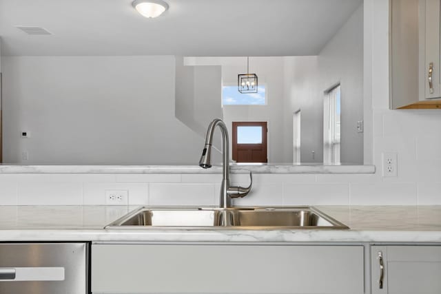 kitchen featuring dishwasher, a sink, decorative backsplash, and light stone countertops