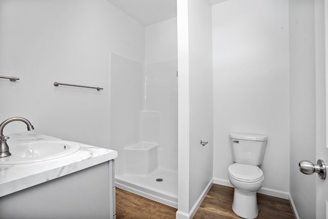 bathroom featuring toilet, a shower, wood finished floors, and baseboards
