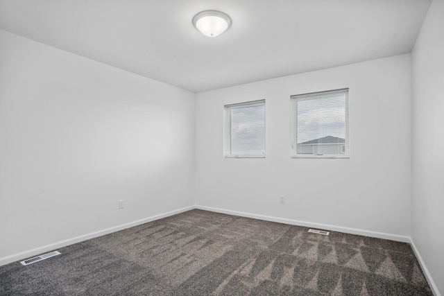 spare room featuring visible vents, dark carpet, and baseboards