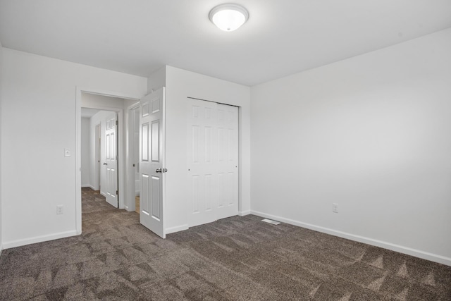unfurnished bedroom featuring baseboards, dark carpet, and a closet