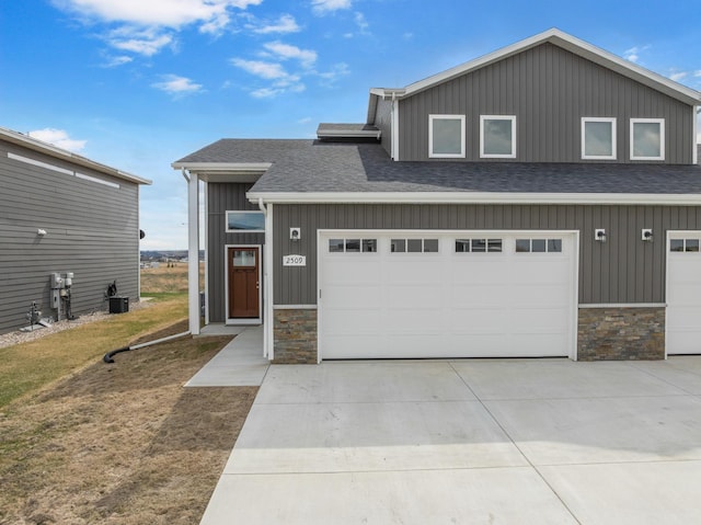 view of front facade with driveway, board and batten siding, stone siding, a shingled roof, and central AC