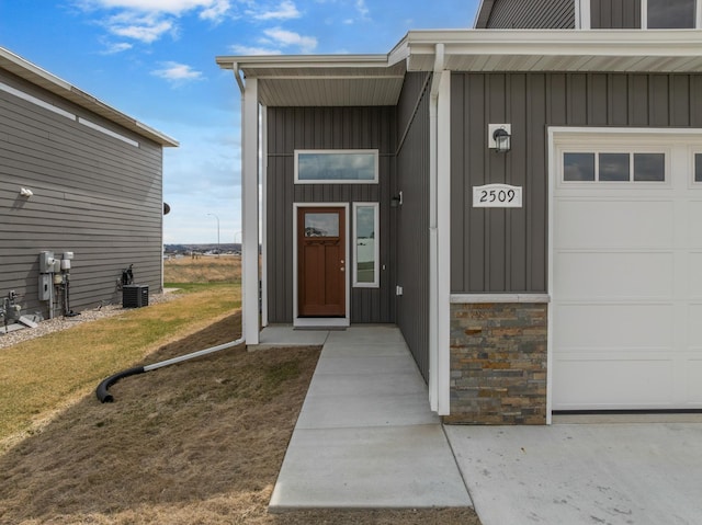 doorway to property featuring a garage, board and batten siding, and central AC