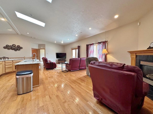 living area featuring a tile fireplace, light wood-type flooring, recessed lighting, and vaulted ceiling with skylight