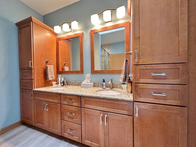 full bath with double vanity, a sink, wood finished floors, and baseboards