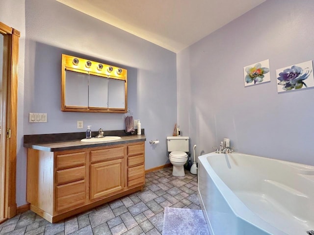 bathroom featuring a washtub, stone finish flooring, toilet, vanity, and baseboards