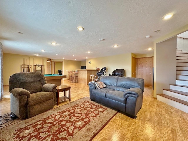 living area with a textured ceiling, bar, light wood finished floors, pool table, and stairs