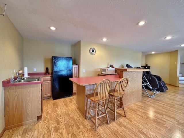 kitchen featuring a sink, a breakfast bar area, white microwave, light wood-style flooring, and freestanding refrigerator