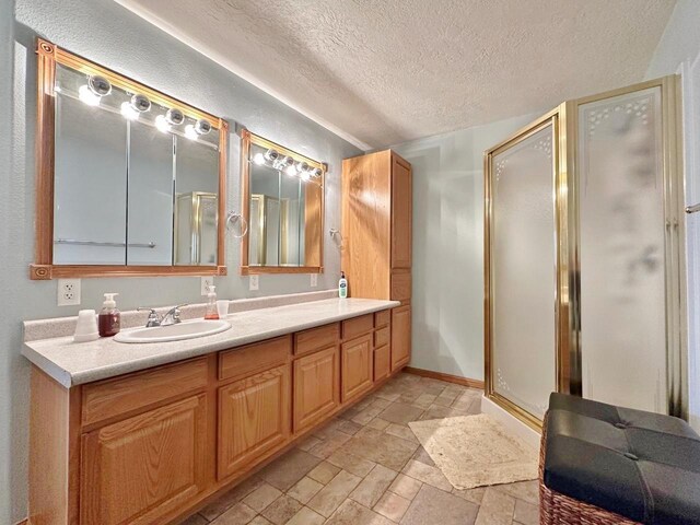 bathroom with stone tile floors, a textured ceiling, a sink, and a shower stall
