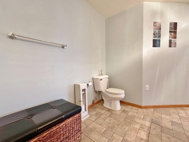 half bath with stone tile floors, baseboards, and toilet
