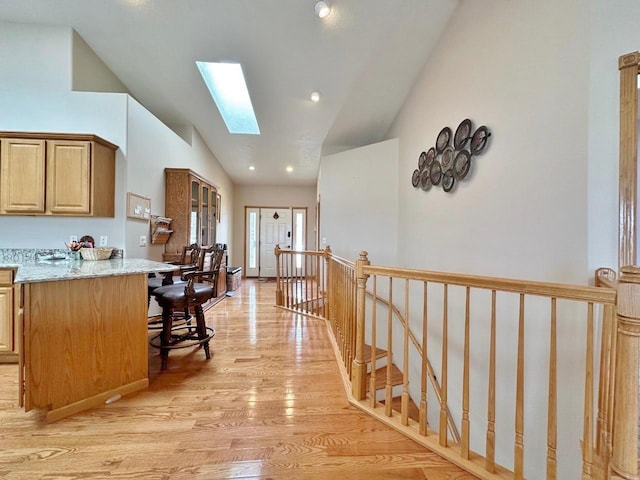 kitchen featuring light wood finished floors, recessed lighting, lofted ceiling with skylight, a breakfast bar area, and light stone counters