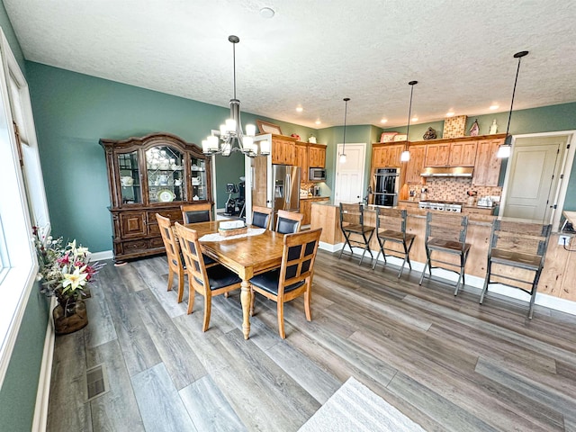 dining area with a textured ceiling, visible vents, wood finished floors, and a chandelier