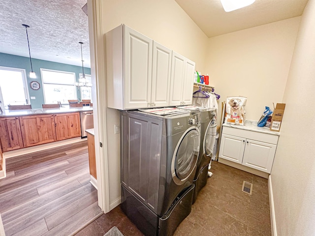 washroom with wood finished floors, cabinet space, washing machine and dryer, visible vents, and a textured ceiling