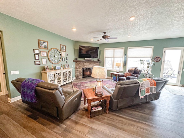 living area with a textured ceiling, wood finished floors, a wealth of natural light, and a ceiling fan