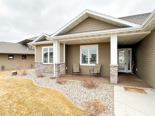 exterior space with a porch, a shingled roof, and stone siding
