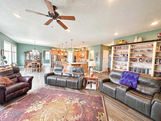 living area featuring baseboards, wood finished floors, ceiling fan with notable chandelier, and a textured ceiling