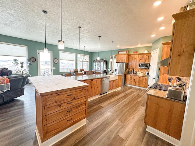 kitchen featuring appliances with stainless steel finishes, a textured ceiling, wood finished floors, and a large island with sink