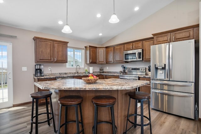 kitchen with a sink, light wood finished floors, stainless steel appliances, lofted ceiling, and a kitchen island