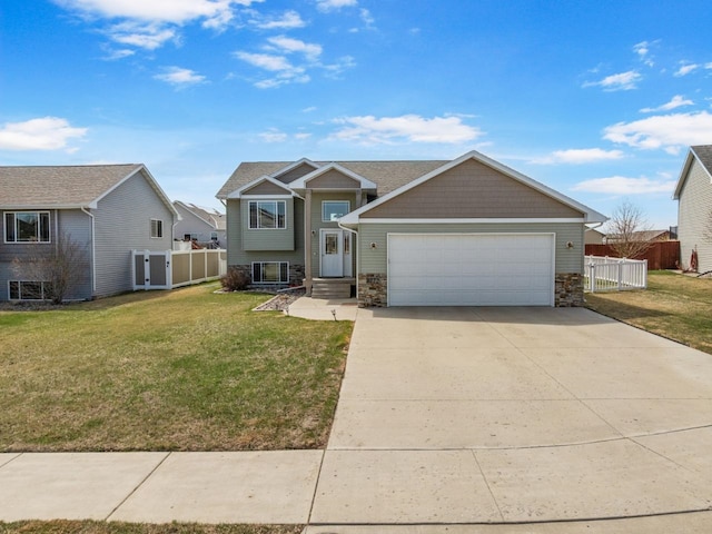 tri-level home with an attached garage, a front lawn, fence, and stone siding