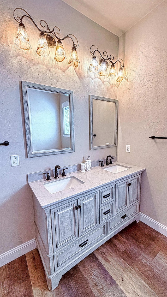 full bathroom with a sink, baseboards, double vanity, and wood finished floors