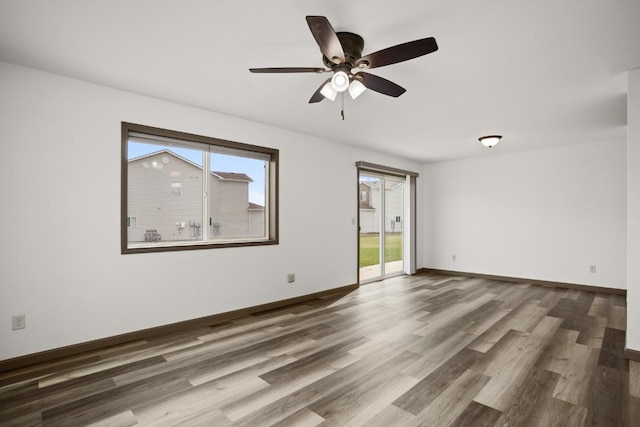 spare room with baseboards, a ceiling fan, wood finished floors, and a healthy amount of sunlight