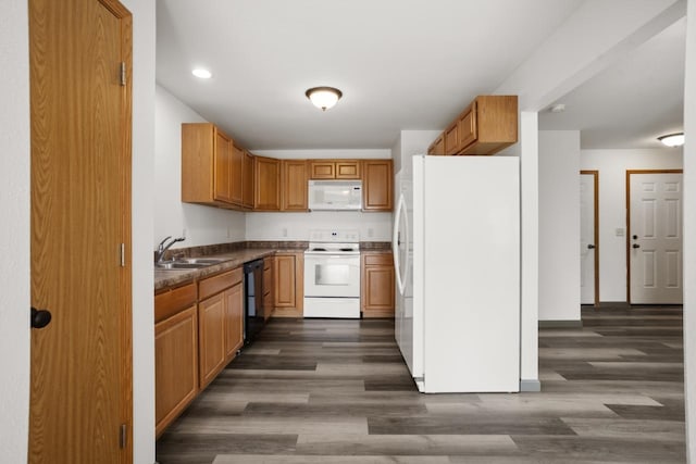 kitchen with dark countertops, a sink, white appliances, dark wood finished floors, and recessed lighting