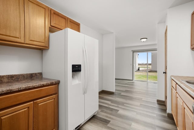 kitchen featuring dark countertops, baseboards, a sink, light wood-style flooring, and white fridge with ice dispenser
