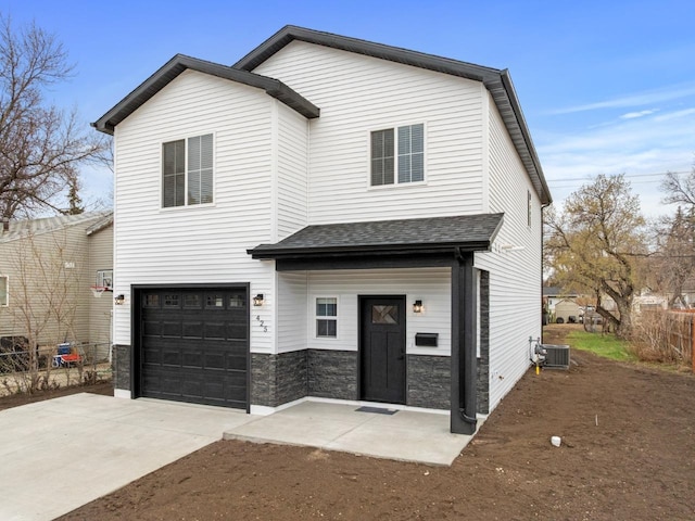 view of front of property with a garage, central AC, fence, concrete driveway, and stone siding