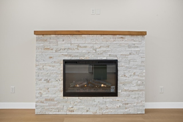 room details with baseboards, wood finished floors, and a stone fireplace