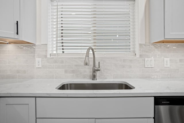 kitchen featuring tasteful backsplash, stainless steel dishwasher, a sink, light stone counters, and white cabinets