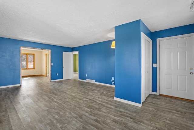 unfurnished living room featuring visible vents, a textured ceiling, baseboards, and wood finished floors