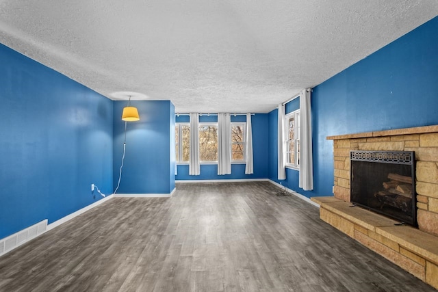 unfurnished living room featuring a stone fireplace, a textured ceiling, visible vents, wood finished floors, and baseboards