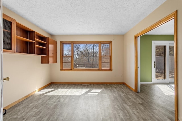 spare room featuring baseboards, a textured ceiling, and wood finished floors