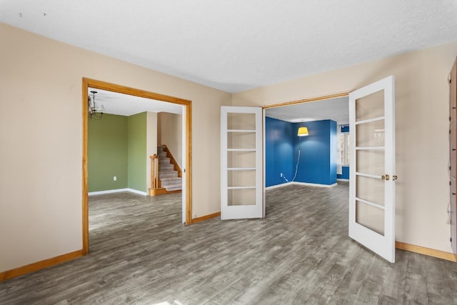 unfurnished room featuring french doors, stairs, baseboards, and wood finished floors