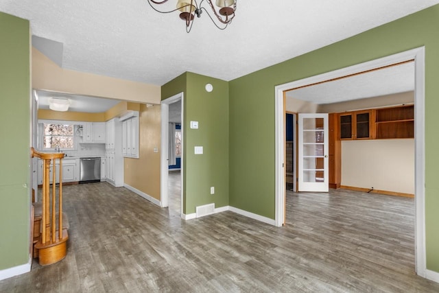 unfurnished living room with visible vents, wood finished floors, a sink, baseboards, and an inviting chandelier
