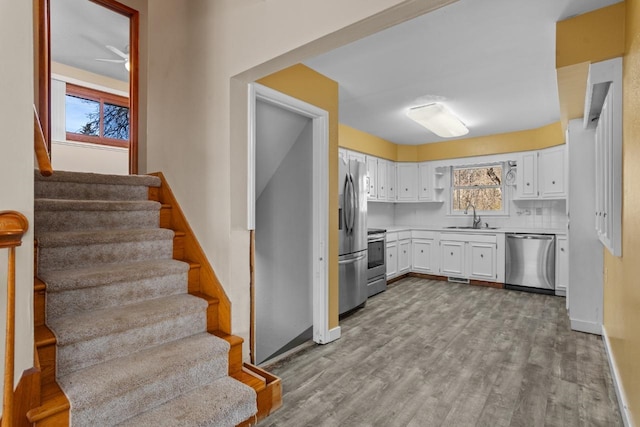 kitchen featuring a sink, appliances with stainless steel finishes, wood finished floors, and white cabinetry