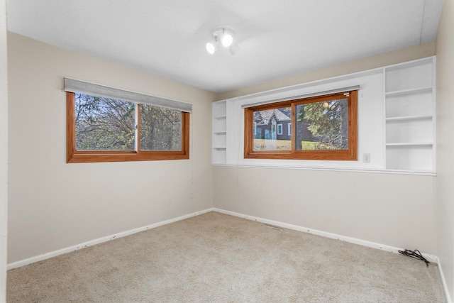 carpeted spare room featuring built in features and baseboards