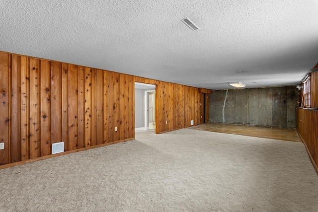 finished below grade area featuring wooden walls, a textured ceiling, visible vents, and light carpet
