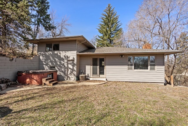 rear view of house with a chimney, roof with shingles, a lawn, a patio area, and a hot tub