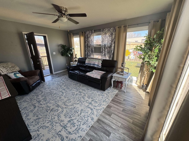 living area featuring plenty of natural light, a ceiling fan, baseboards, and wood finished floors