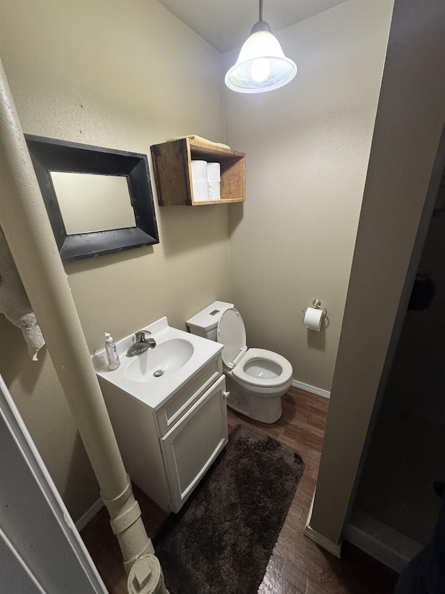 bathroom featuring toilet, baseboards, wood finished floors, and vanity