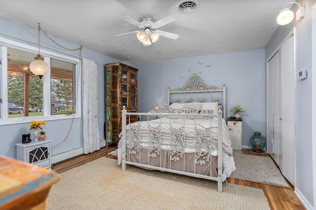 9500 135th Ave, Sawyer, ND 58781 - bedroom with visible vents, a closet, wood finished floors, a baseboard heating unit, and a ceiling fan