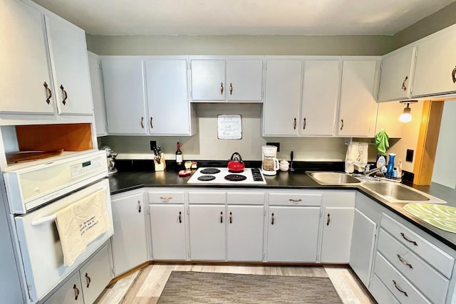 kitchen with dark countertops, light wood-type flooring, white appliances, and white cabinetry