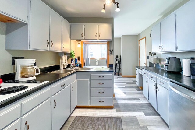 kitchen featuring white electric cooktop, dark countertops, stainless steel dishwasher, a sink, and light wood-style flooring