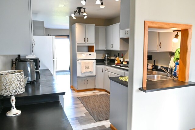 kitchen with dark countertops, light wood-type flooring, a sink, white cabinets, and white appliances